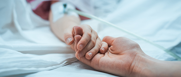 Recovering Little Child Lying in the Hospital Bed Sleeping, Mother Holds Her Hand Comforting. Focus on the Hands. Emotional Family Moment.