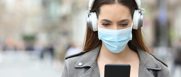 Girl with mask and headphones reads phone in the street