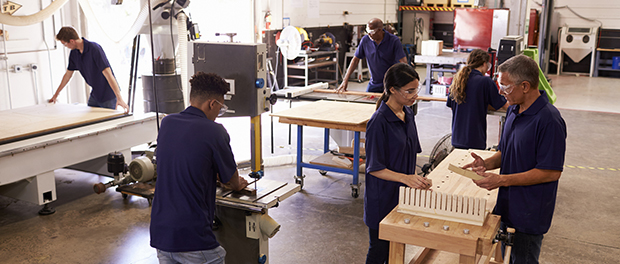 Carpenters Working On Machines In Busy Woodworking Workshop